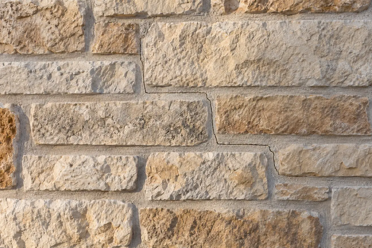 Narrow crack stepping along the mortar joints of a cream and tan limestone wall